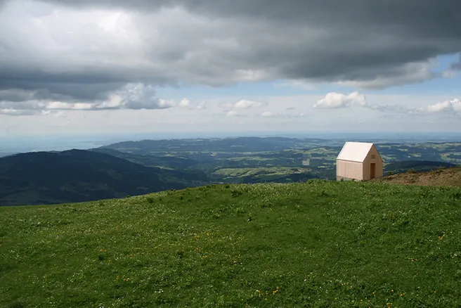 Hügelige Landschaft, kleine Holzkapelle auf grüner Wiese 