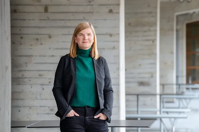 Porträt von Katja Thoring. Sie trägt einen dunkel grünen Rollkragenpullover und einen Blazer. Das blonde Haar trägt sie offen und schaut lächelnd in die Kamera. 